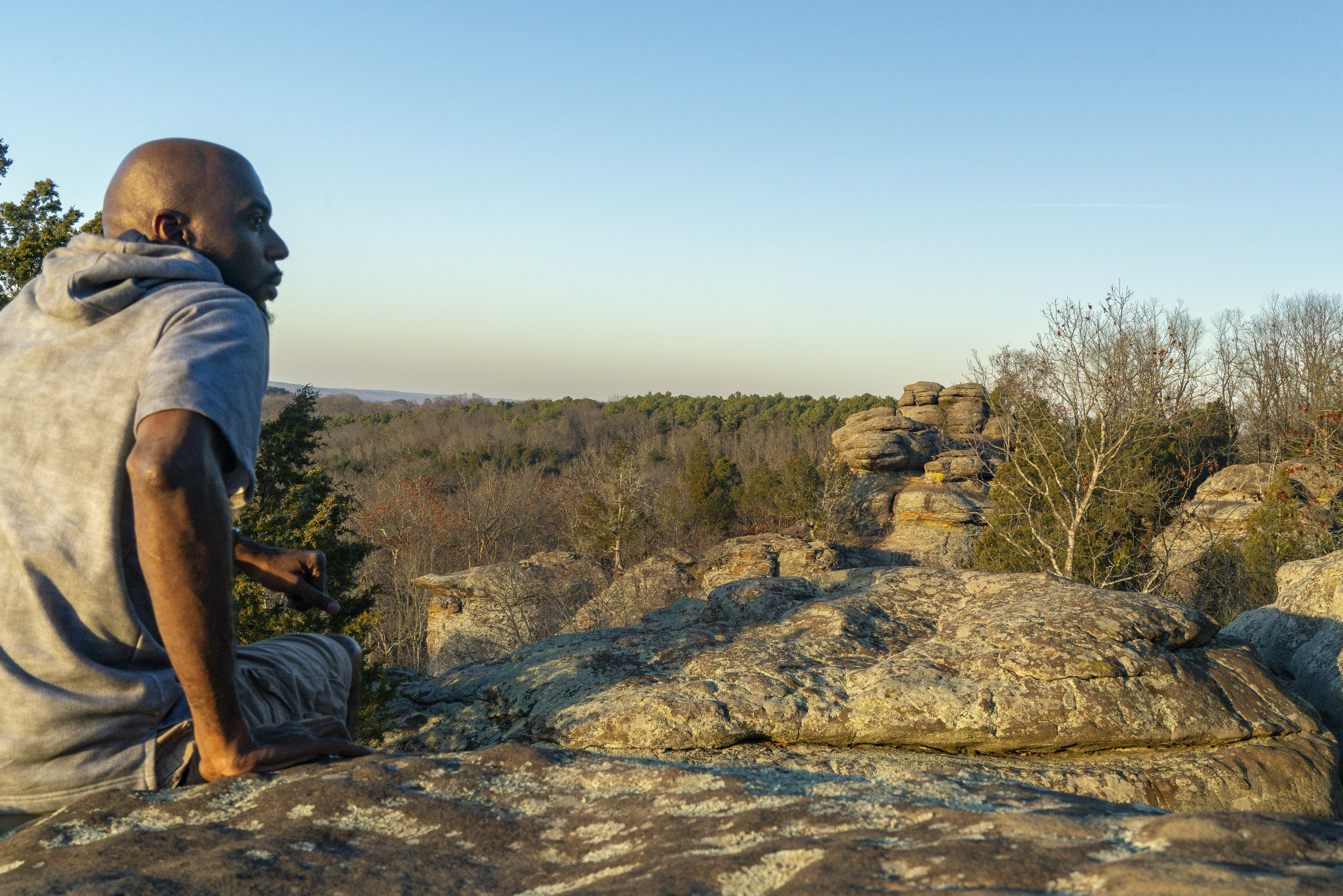 a man sitting on top of a rock next to a forest