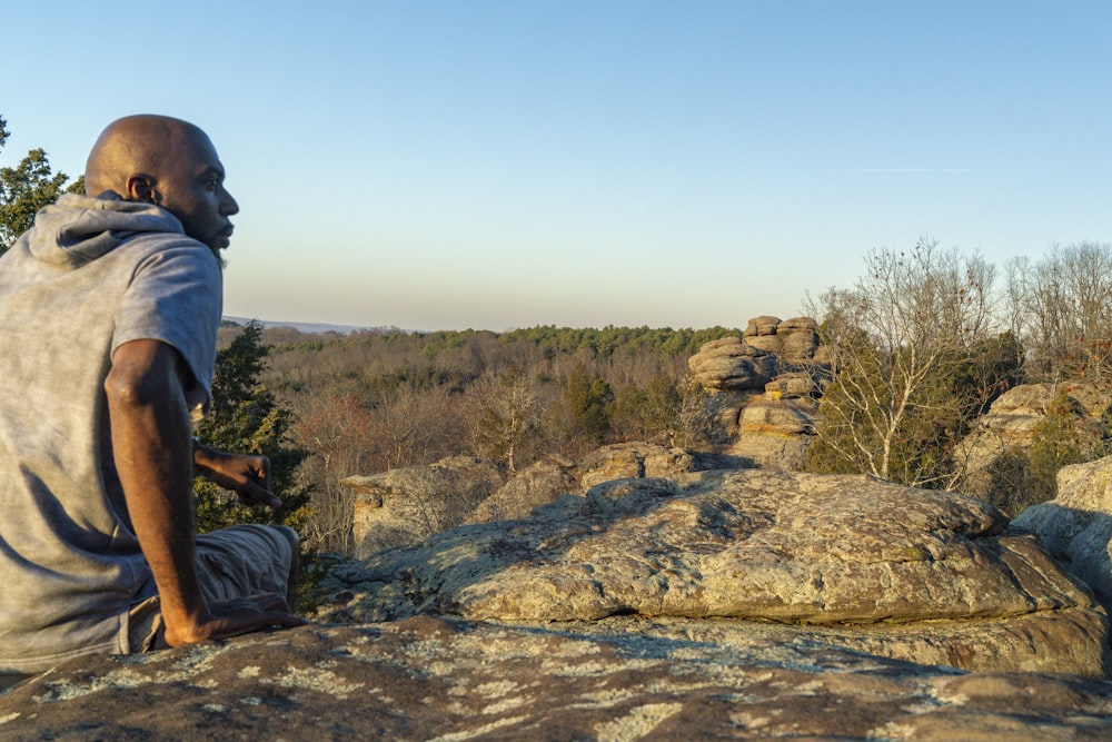 a man sitting on top of a rock next to a forest