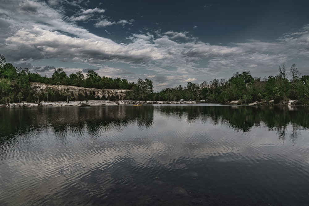 a body of water surrounded by trees under a cloudy sky