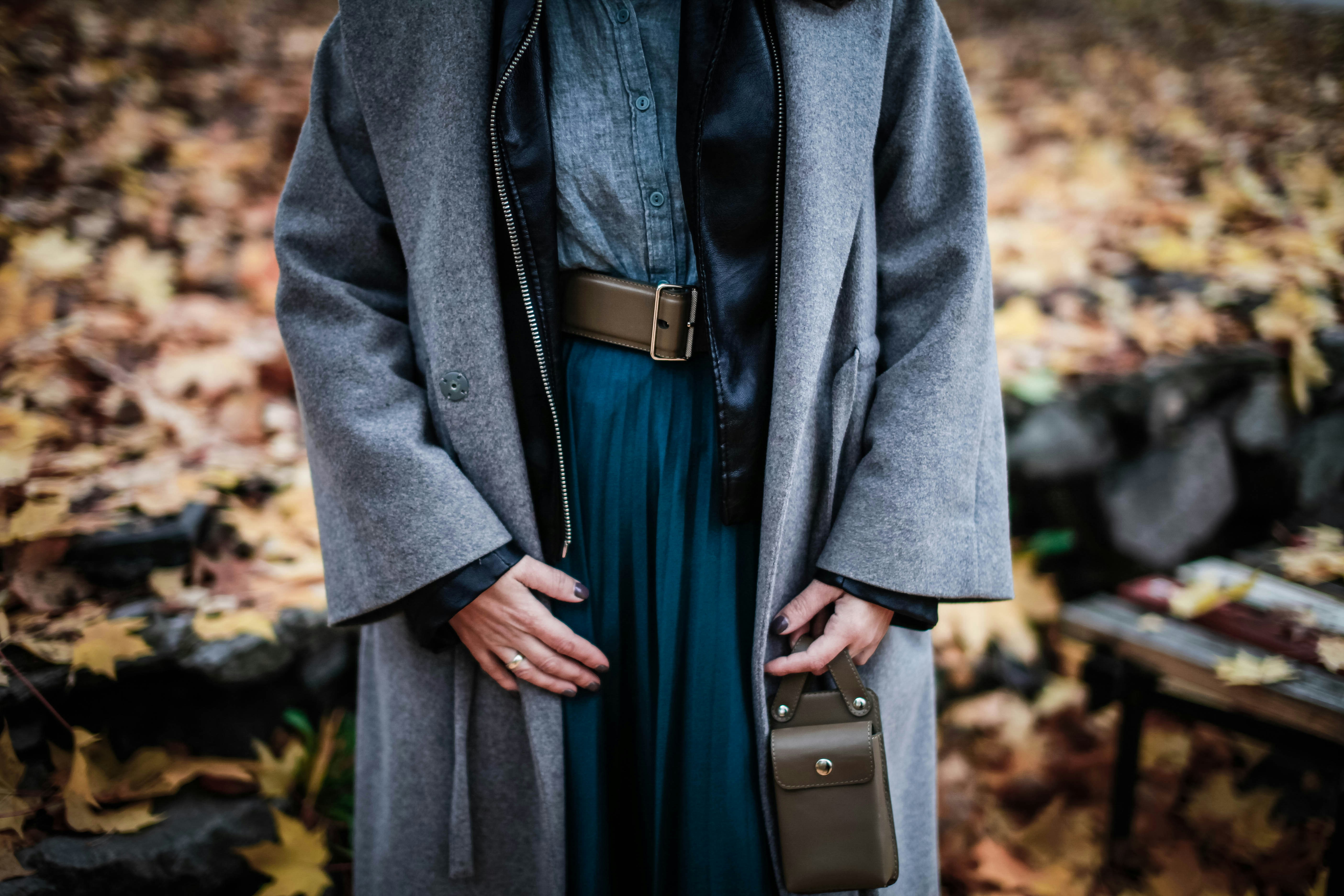a woman wearing a coat and a dress standing in leaves