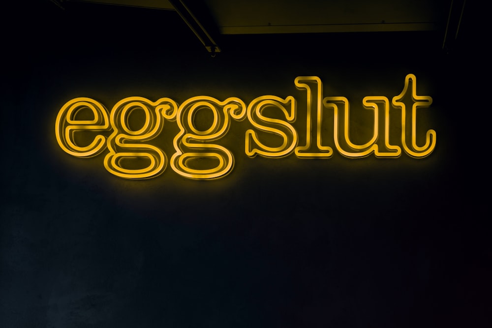a neon sign that says eggslut on a black wall
