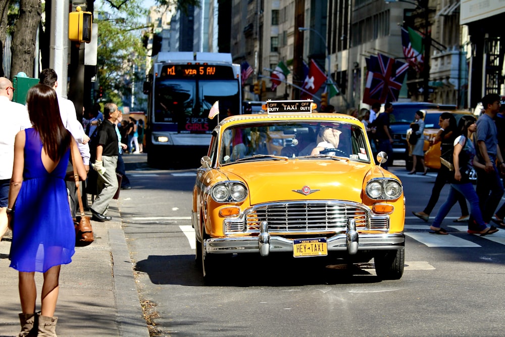 a yellow taxi driving down a street next to a crowd of people