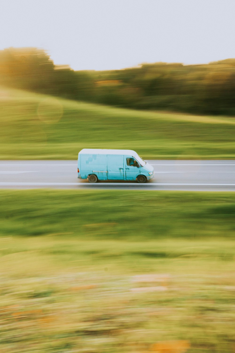 a blue van driving down a road next to a lush green field