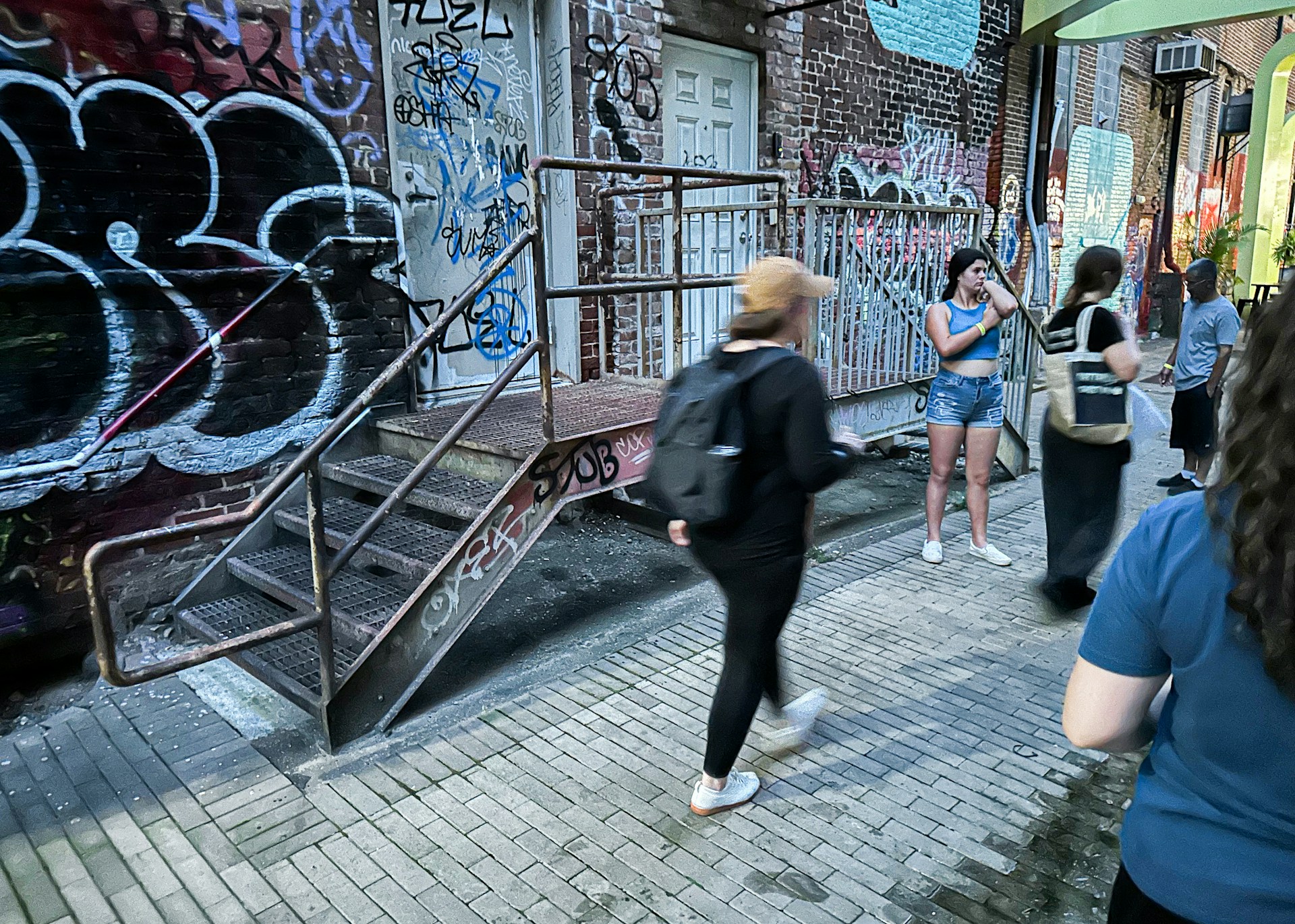 A vibrant urban scene featuring a diverse group of young people wearing stylish streetwear in a graffiti-filled alley.