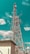 A tall communication tower stands against a vibrant teal sky, with scattered clouds adding texture to the background. The tower is surrounded by utility lines and a small fenced building marked with the number 169. The tower's structure is intricate, featuring various antennas and dish equipment.