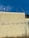 A beige wall with graffiti text reading 'JESUS TA VOLTANDO' in black letters. The top of the wall features a few antennas against a blue sky with scattered clouds.