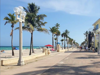 Tourists enjoying a sunny beachside promenade with palm trees and blue waters.