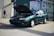A friendly salesperson talking on the phone next to a parked car.