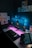 A modern computer setup featuring a large monitor with an image of a house in a mountainous landscape on the screen. The desk is illuminated by neon pink and blue lighting, which creates a futuristic atmosphere. A keyboard and mouse are positioned on the desk along with a laptop displaying an image. The walls are decorated with various art posters and designs.