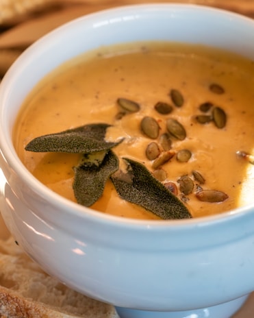 A steaming bowl of creamy pumpkin soup garnished with roasted seeds and a swirl of cream.