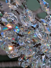 Sparkling crystal stones reflecting light in a prismatic display, creating a rainbow effect. The crystals are arranged closely, with metallic fixtures visible, suggesting they are part of a decorative item like a chandelier.