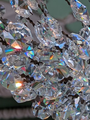Sparkling crystal stones reflecting light in a prismatic display, creating a rainbow effect. The crystals are arranged closely, with metallic fixtures visible, suggesting they are part of a decorative item like a chandelier.