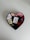 A heart-shaped box contains neatly arranged colorful ribbon rolls in a gradient from white and beige to various shades of pink and red. In the center of the box is a small white card featuring a printed red heart, accompanied by cursive text.