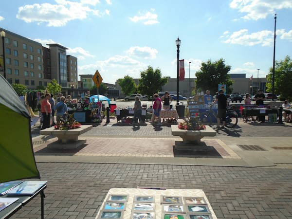 Visitors browsing framed artwork on a table at an outdoor juried art festival