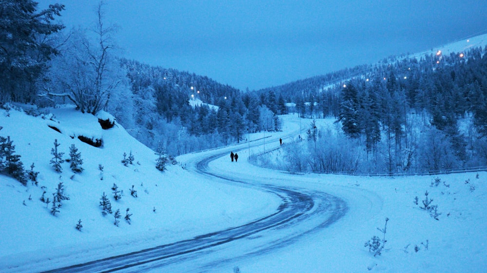 a couple of people walking down a snow covered road