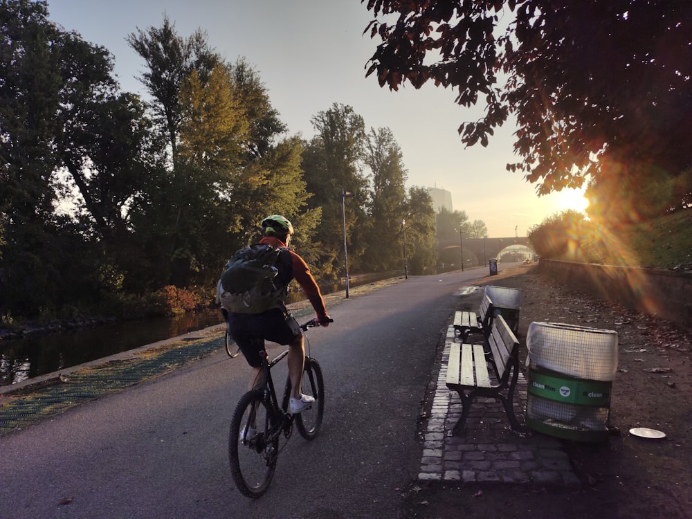 um homem andando de bicicleta por uma rua ao lado de um banco de parque