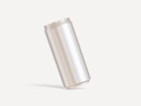 A plain, metallic cylindrical can is positioned on a light background, creating a minimalist and clean aesthetic.