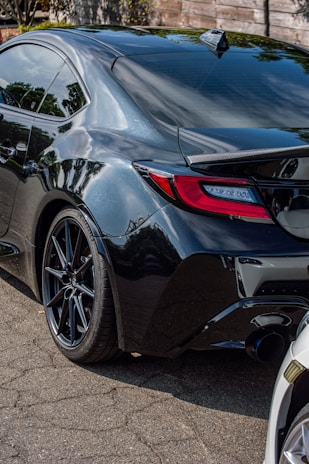 Side profile of a BMW with a custom performance exhaust, parked on a dark asphalt surface with reflections.