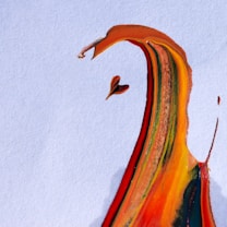 A splash of vibrant paint, creating an abstract form on a textured white background. The colors blend seamlessly, with sweeping lines and curves that evoke the shape of a bird in flight or an expressive figure.