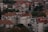 A cluster of residential buildings with red-tiled roofs surrounded by trees and vegetation. The structures vary in height and feature multiple windows and balconies. The greenery adds a natural element to the urban landscape, giving a blend of architecture and nature.