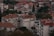 A cluster of residential buildings with red-tiled roofs surrounded by trees and vegetation. The structures vary in height and feature multiple windows and balconies. The greenery adds a natural element to the urban landscape, giving a blend of architecture and nature.