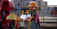 A joyful clown with bright red nose entertaining a group of laughing children under a big blue and red balloon arch.