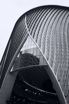 A modern architectural structure with a sweeping curved design and intricate facade patterns. The building features a combination of glass and metal elements, reflecting an innovative and futuristic aesthetic.