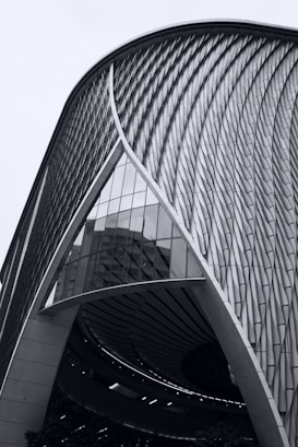 A modern architectural structure with a sweeping curved design and intricate facade patterns. The building features a combination of glass and metal elements, reflecting an innovative and futuristic aesthetic.