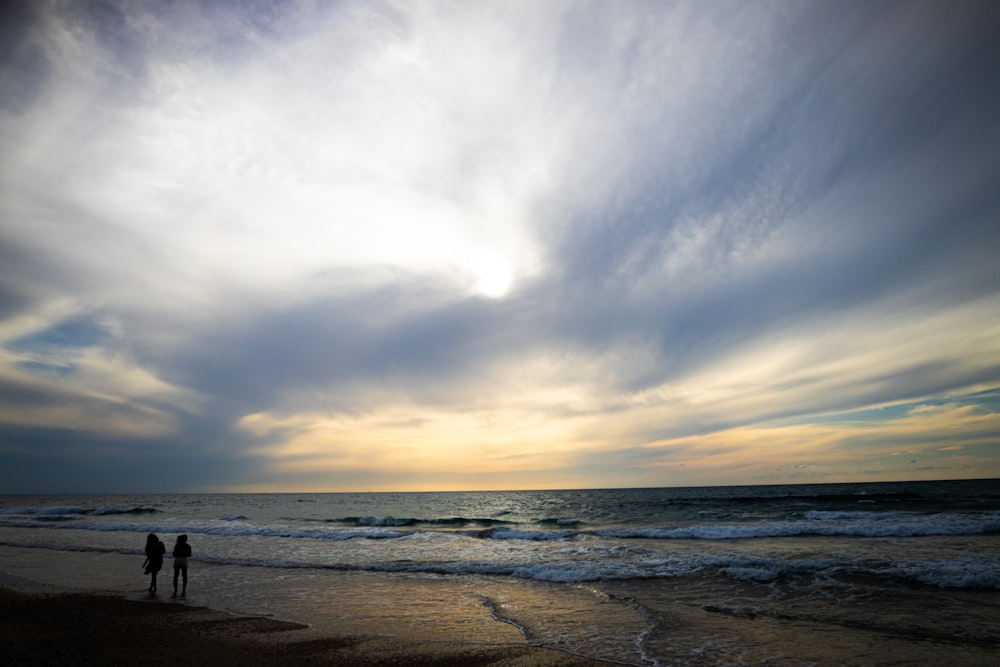 two people standing on a beach near the ocean