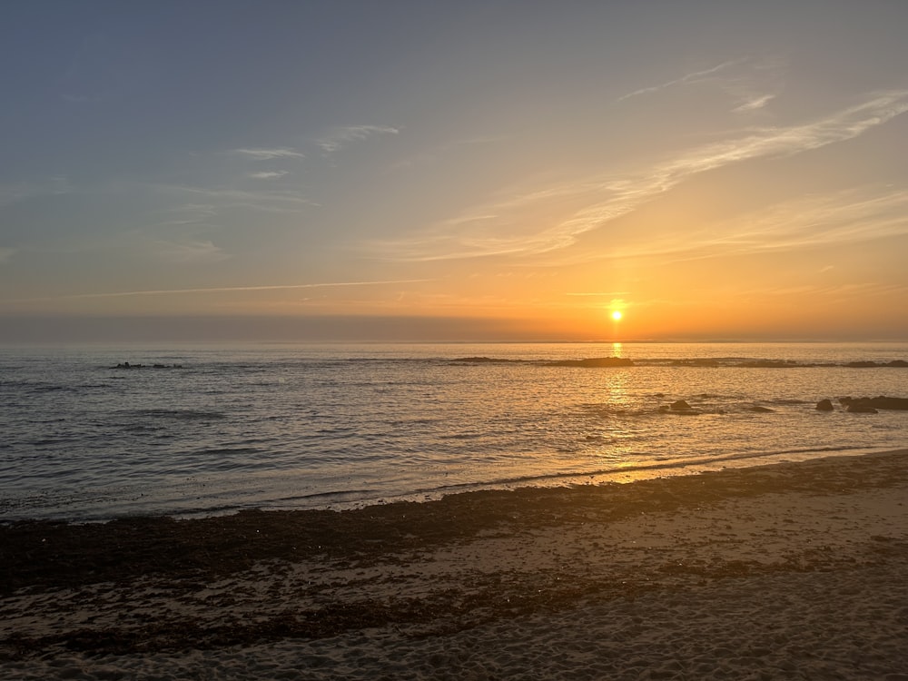 the sun is setting over the water on the beach