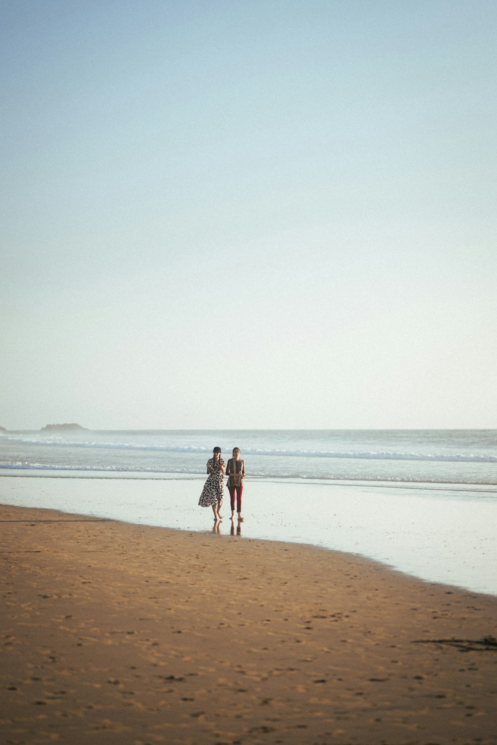 two people walking on the beach with a surfboard