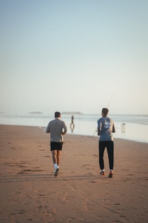 Runners jogging on a sandy beach at sunrise with waves gently crashing by