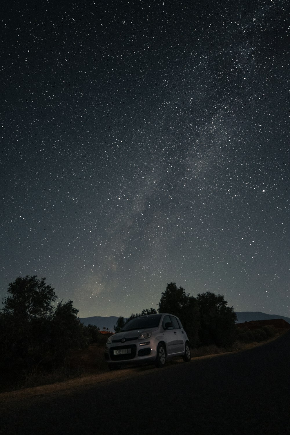 a car parked on the side of a road under a night sky filled with stars