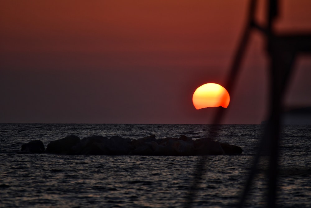 the sun is setting over the ocean with rocks in the foreground