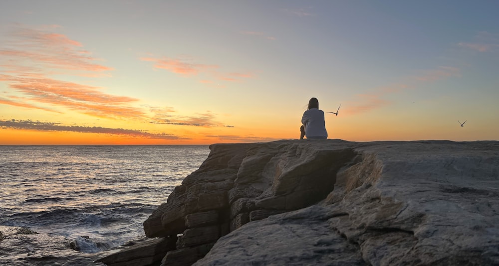 a person sitting on top of a rock next to the ocean