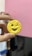 A hand is holding a small round cracker with a smiling and winking face design. The background includes shelves and a pink wall.