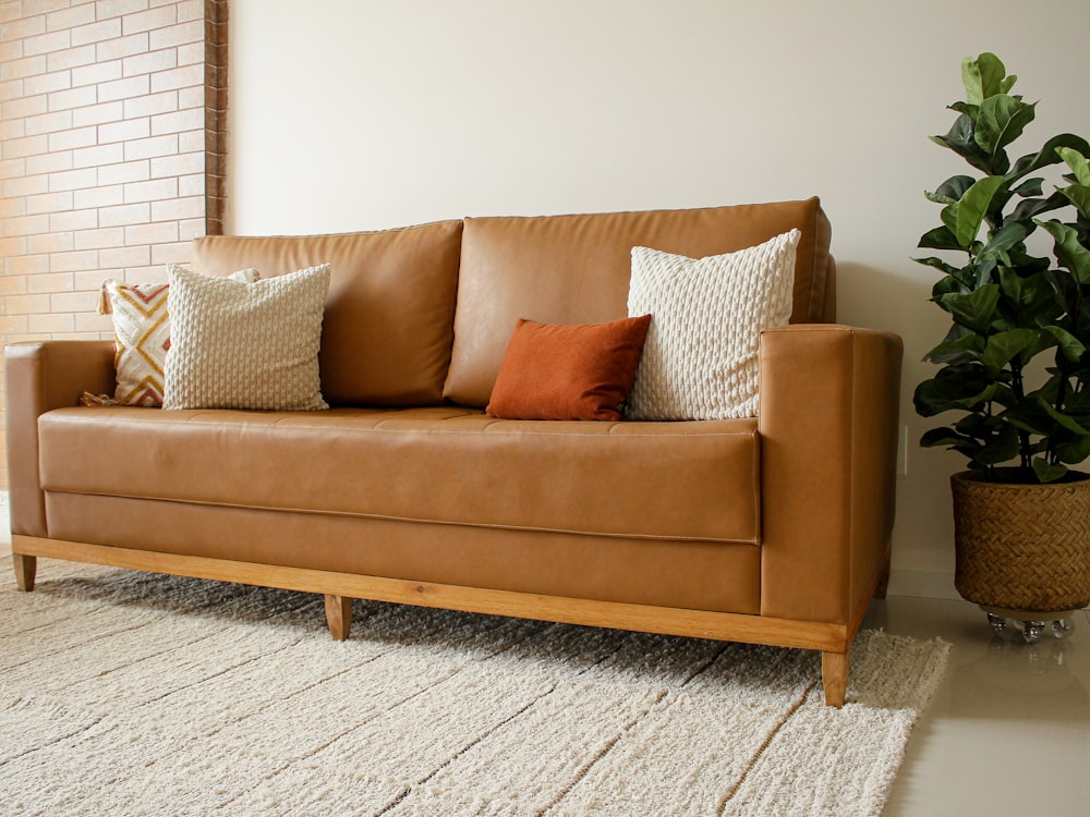 a brown leather couch sitting in a living room next to a potted plant