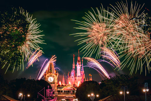 Vista nocturna del castillo iluminado en Disneyland Paris con fuegos artificiales de fondo.