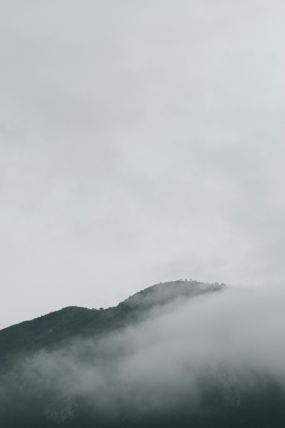 a mountain covered in fog and clouds on a cloudy day