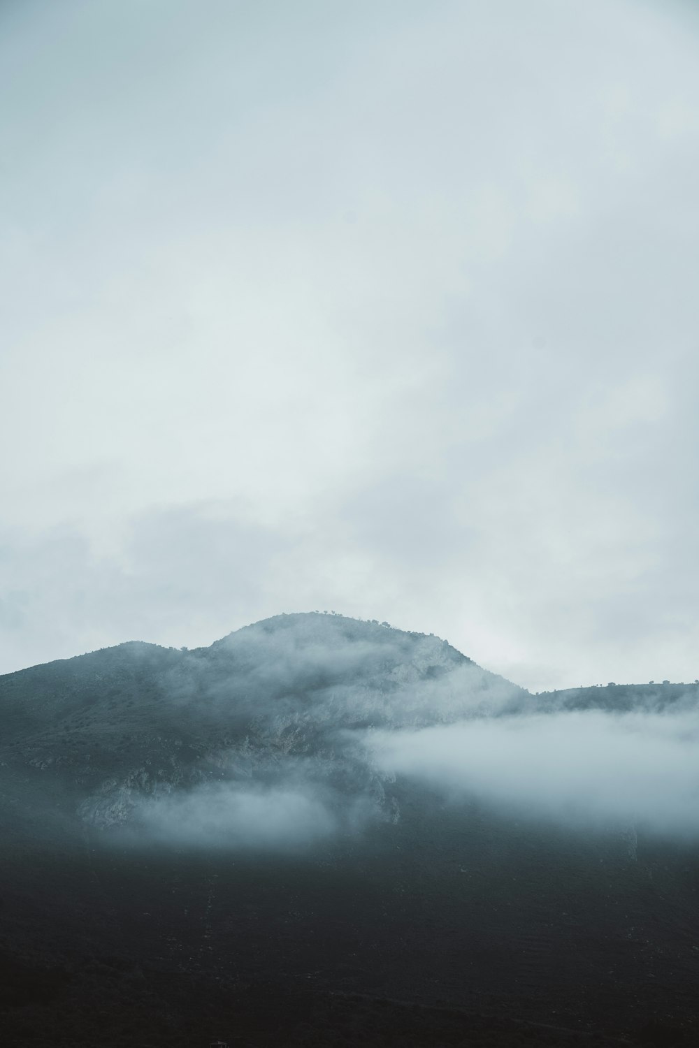 a mountain covered in fog and clouds on a cloudy day