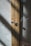 A close-up view of a wooden cabinet with intricate woven mesh panels. The wood has a natural grain, and the cabinet features two circular metallic knobs. Sunlight casts shadows across the textured surface of the mesh, creating a play of light and shadow.