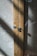 A close-up view of a wooden cabinet with intricate woven mesh panels. The wood has a natural grain, and the cabinet features two circular metallic knobs. Sunlight casts shadows across the textured surface of the mesh, creating a play of light and shadow.