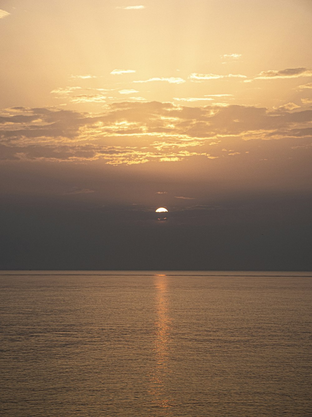 the sun is setting over the ocean on a cloudy day