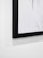 A close-up photo of a framed black ink drawing on paper hanging on a white wall.