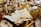 A variety of antique and vintage items are spread across a table. These include old newspapers, brass and glass bottles, ornate figurines, a wire basket filled with spherical objects, and large crystals or minerals. The scene conveys a sense of history and nostalgia.