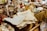 A variety of antique and vintage items are spread across a table. These include old newspapers, brass and glass bottles, ornate figurines, a wire basket filled with spherical objects, and large crystals or minerals. The scene conveys a sense of history and nostalgia.
