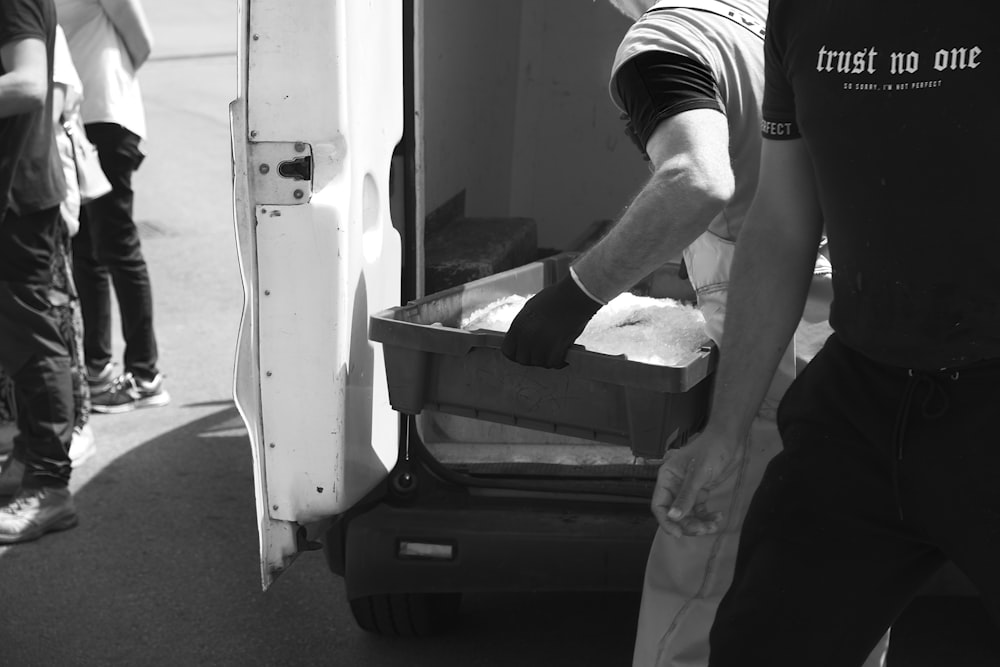 a black and white photo of a man loading something into a truck