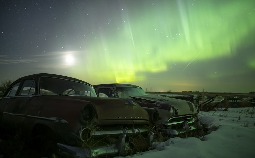 two old cars parked in the snow under a green aurora light