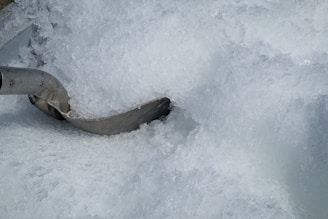 A large pile of crushed ice with a metal scoop partially buried in it. The ice appears translucent and frosty, with varying shades and textures giving a sense of coldness.