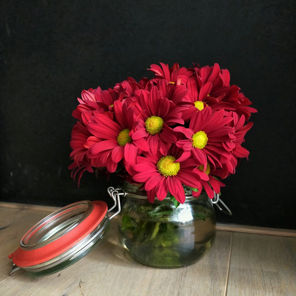 a vase filled with red flowers sitting on top of a wooden table